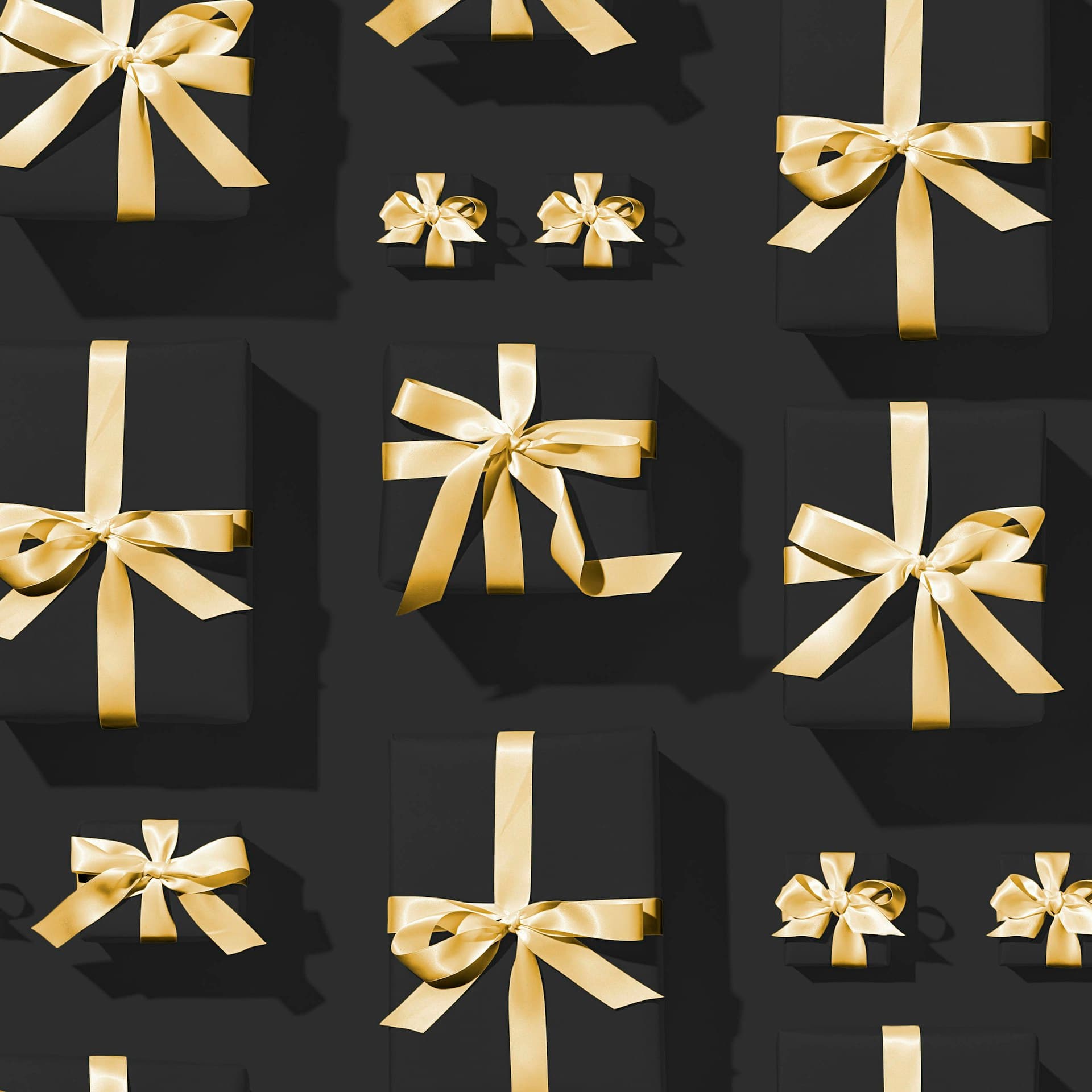 Gift boxes tied with gold ribbon, arranged on a dark surface
